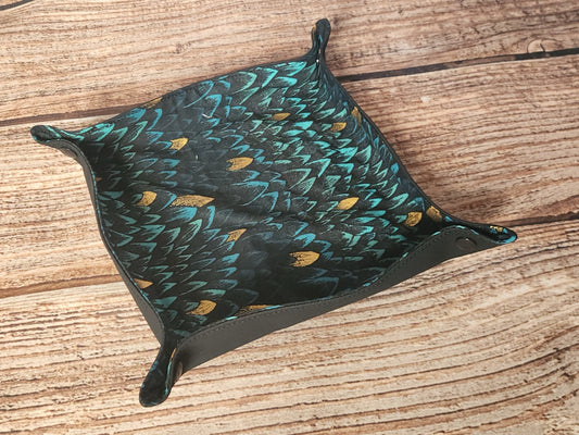 Empty handmade dice tray in teal and black dragon-scale fabric with metallic gold accents, shaped into a shallow catchall tray with snapped corners and black edge trim.